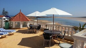 Una terraza con vistas al mar, con sillones de descanso, una mesa y sombrillas.
