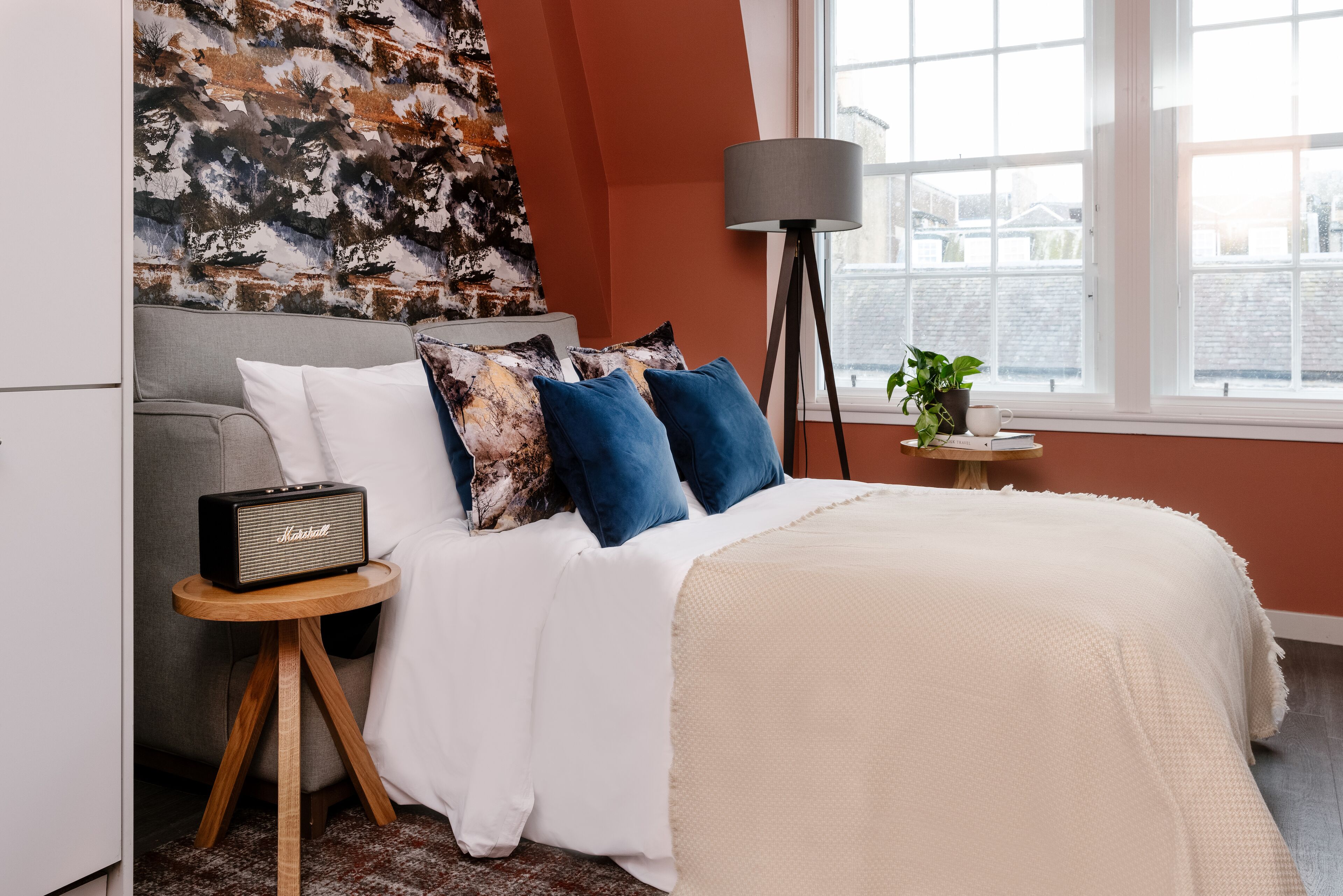 Quarto com cama, rádio sobre uma mesa de cabeceira, abajur e janela com vista.
