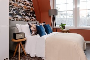 A bedroom with a bed, a radio on a side table, a lamp, and a window with a view.