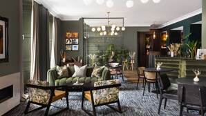 A modern hotel lobby with a green sofa set, a bar area, and a seating area with tables and chairs.