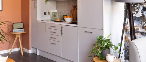 A modern kitchen with white cabinets, a microwave, and a bowl of oranges. There is a small round table with a magazine and a plant.