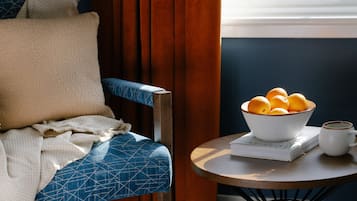A cozy room with a chair, a bowl of oranges, a book, and a cup on a small table.
