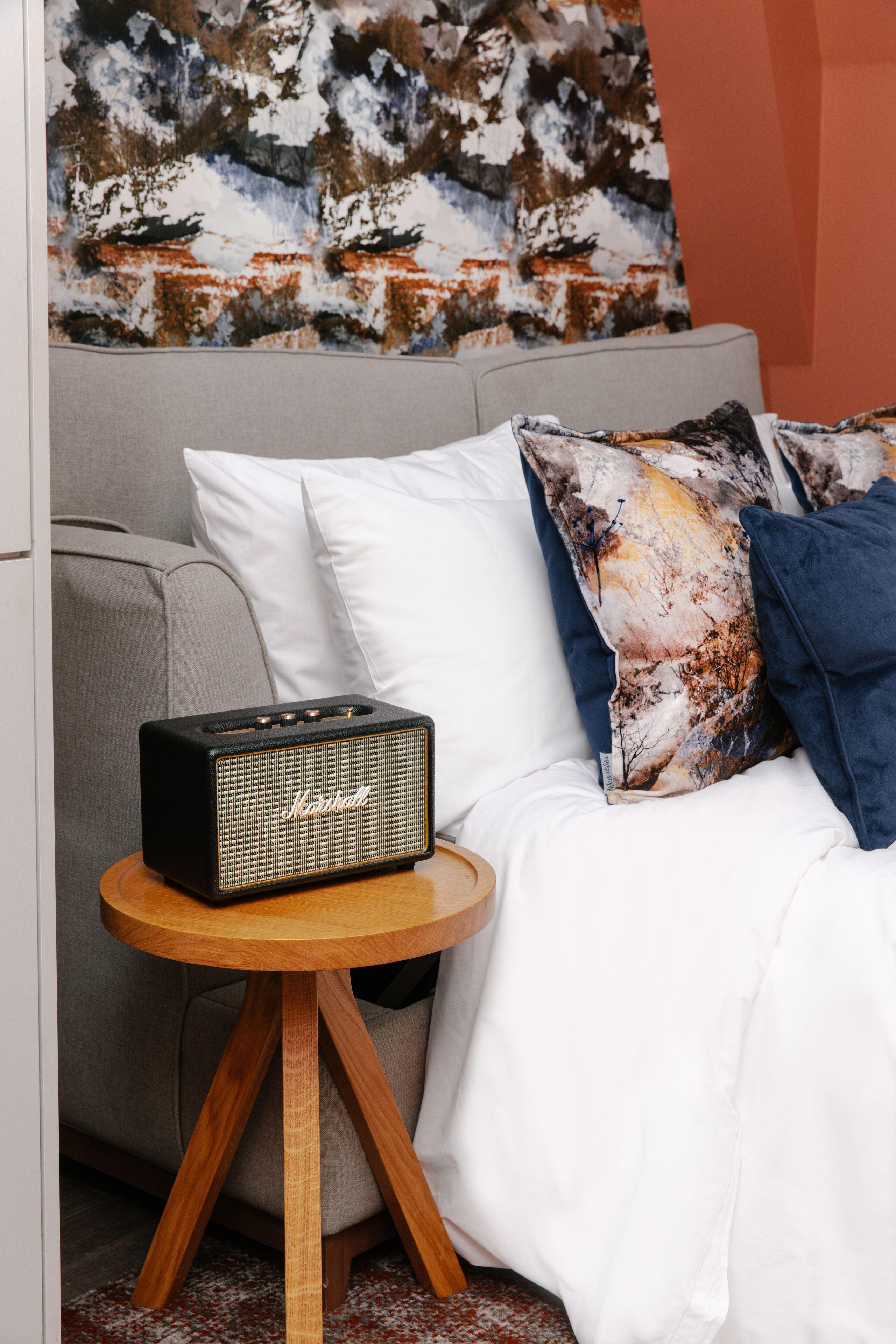 Een bed met witte lakens, een kussen met een patroon en een Marshall-speaker op een houten nachtkastje.