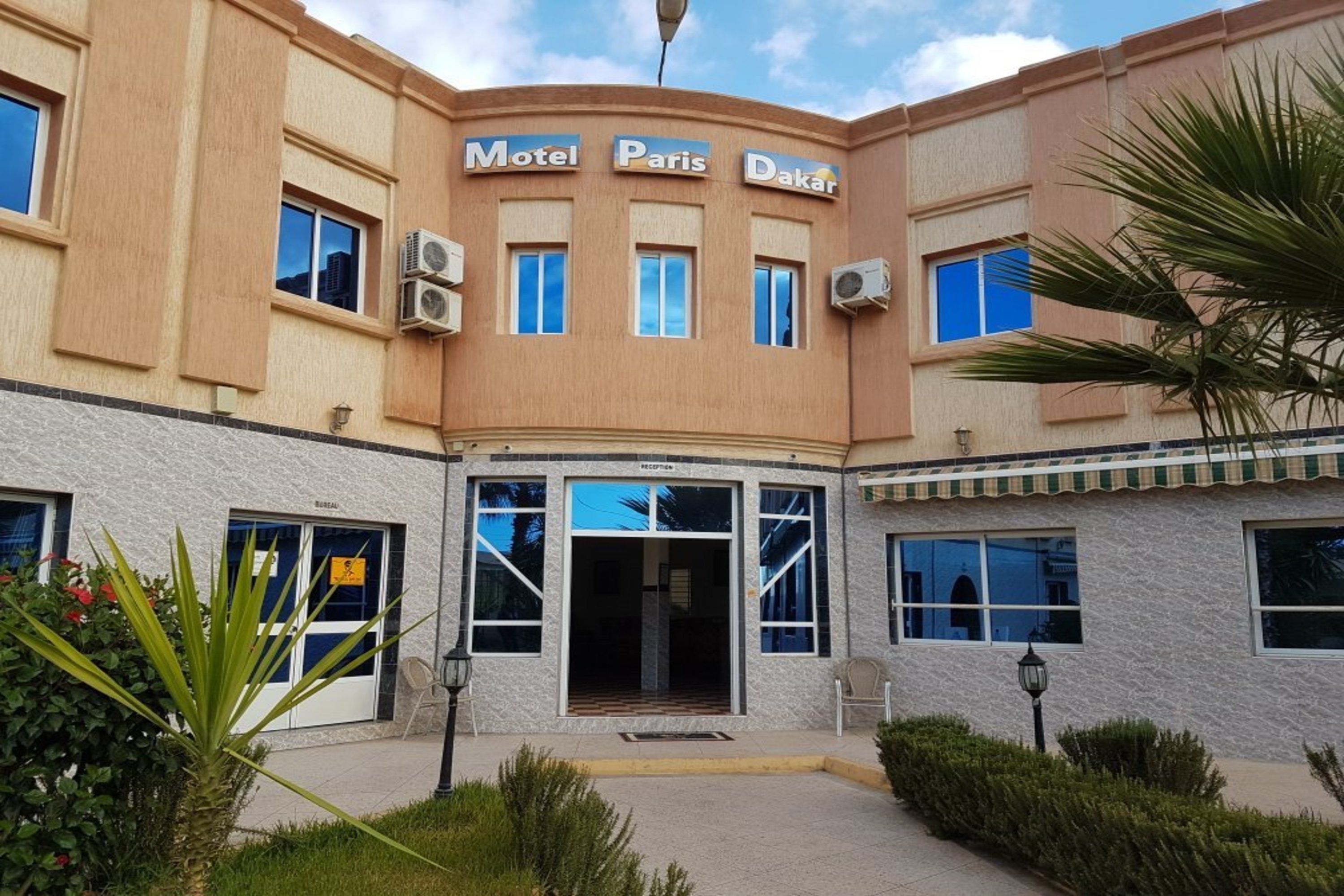 Un bâtiment sur lequel on peut lire l’inscription « Motel Paris Dakar », et un espace d’accueil doté d’une porte en verre.