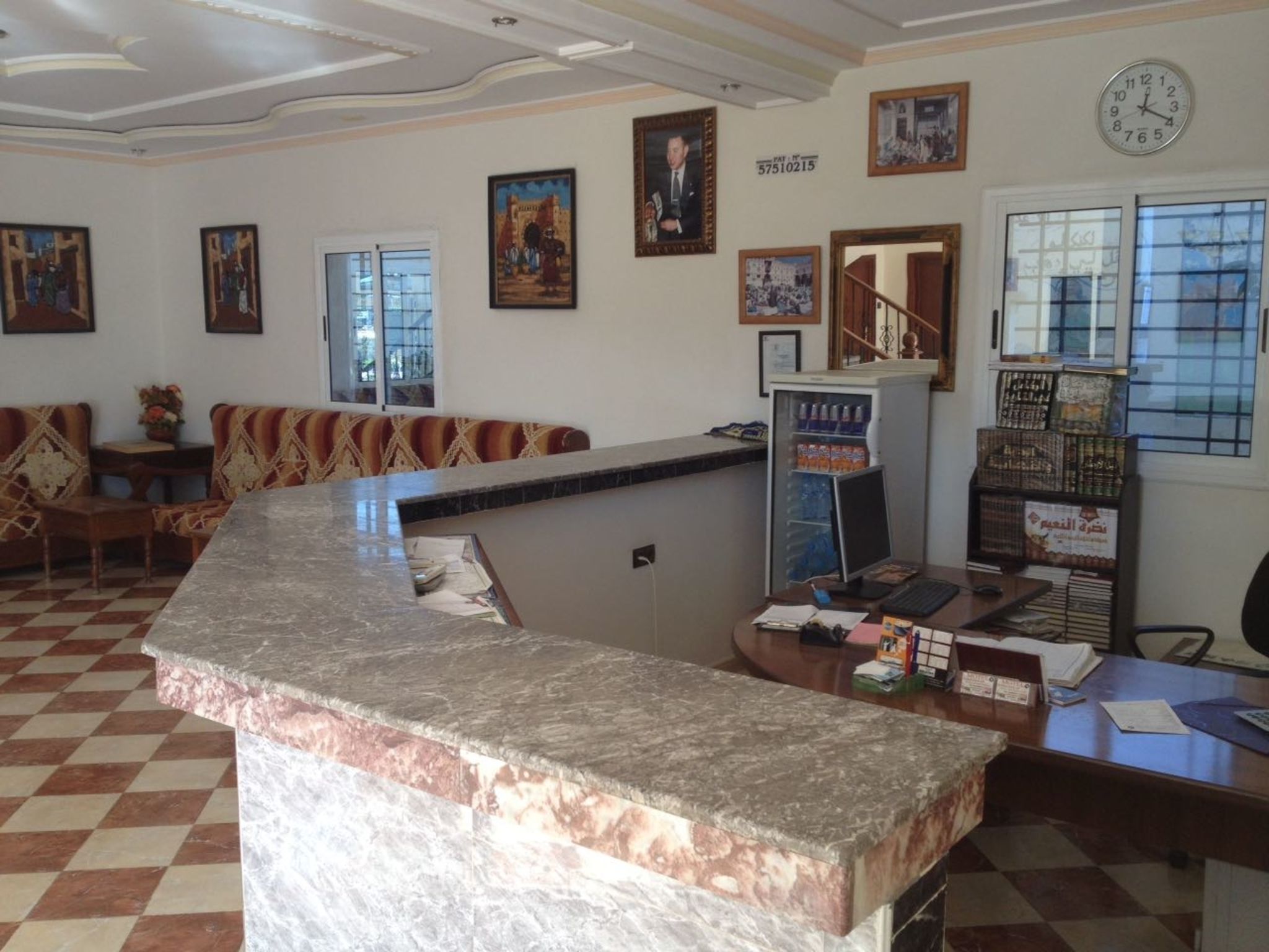 A reception area with a marble counter, a sofa, a refrigerator, and various framed pictures on the walls.