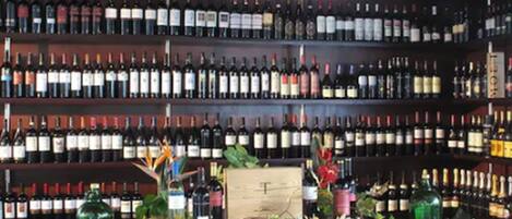 A wine cellar with numerous bottles on shelves, a wooden table with decorative items, and a sign with the letter 'T'.