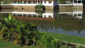 A two-story building with a red roof, white exterior walls, and a reflection in the water. - Resort Monte das Oliveiras (Joanópolis)