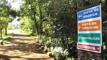 A directional sign with arrows pointing towards 'Pista de Cooper', 'Pista de Aeromodélismo', 'Hortaliças', and 'Fazendinha'.