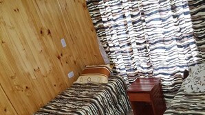 Una stanza con due letti, ognuno rivestito di tessuto a righe. Un poggiatesta in legno su un lato e un piccolo tavolino al centro.