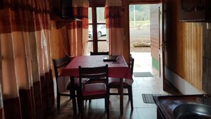 Una baita di legno con un tavolo e sedie, una televisione appesa al muro e una porta che dà sull'esterno.