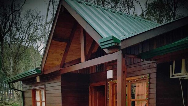 Una baita in legno con tetto spiovente, ingresso in pietra e un piccolo portico.