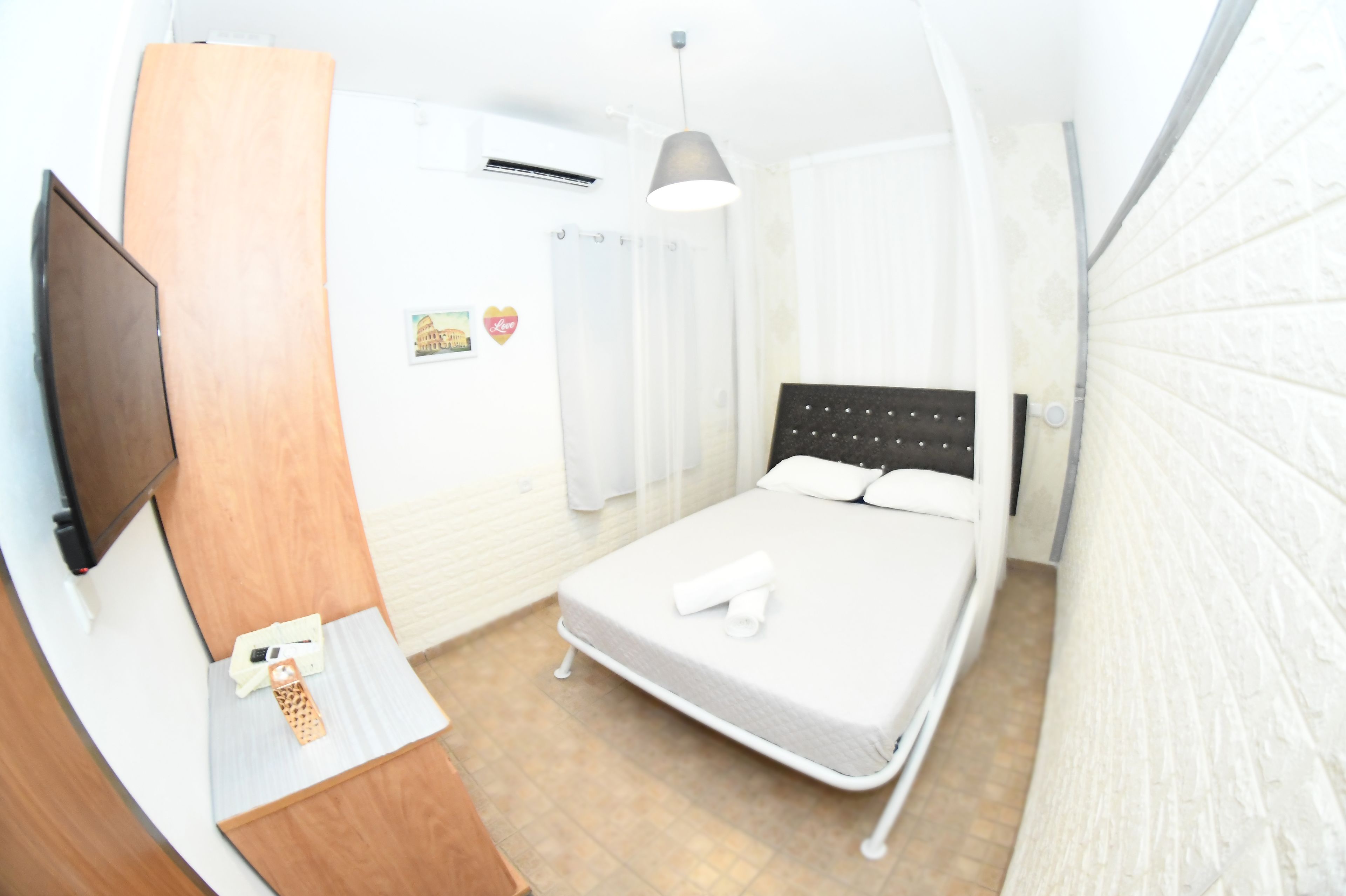Un dormitorio con una cama, televisión, escritorio de madera y pared blanca.