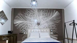 Une chambre à coucher comprenant un lit, une commode, une chaise et une œuvre d’art murale.