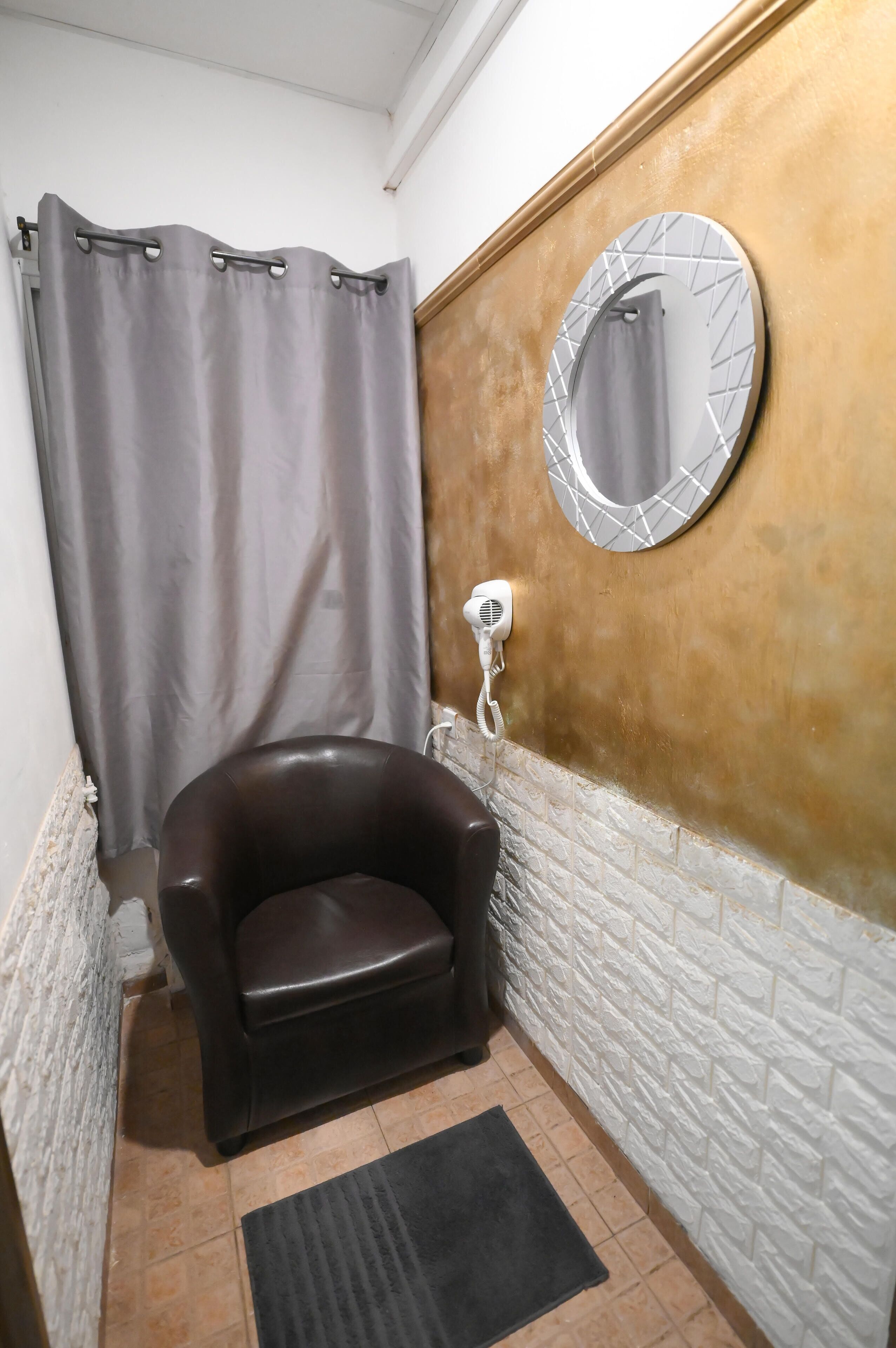 Une salle de bain avec un rideau de douche, un sèche-cheveux, un miroir et une chaise noire.