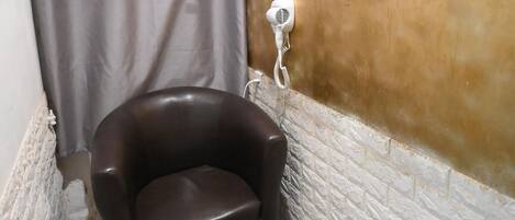 A bathroom with a shower curtain, a hairdryer, a mirror, and a black chair.