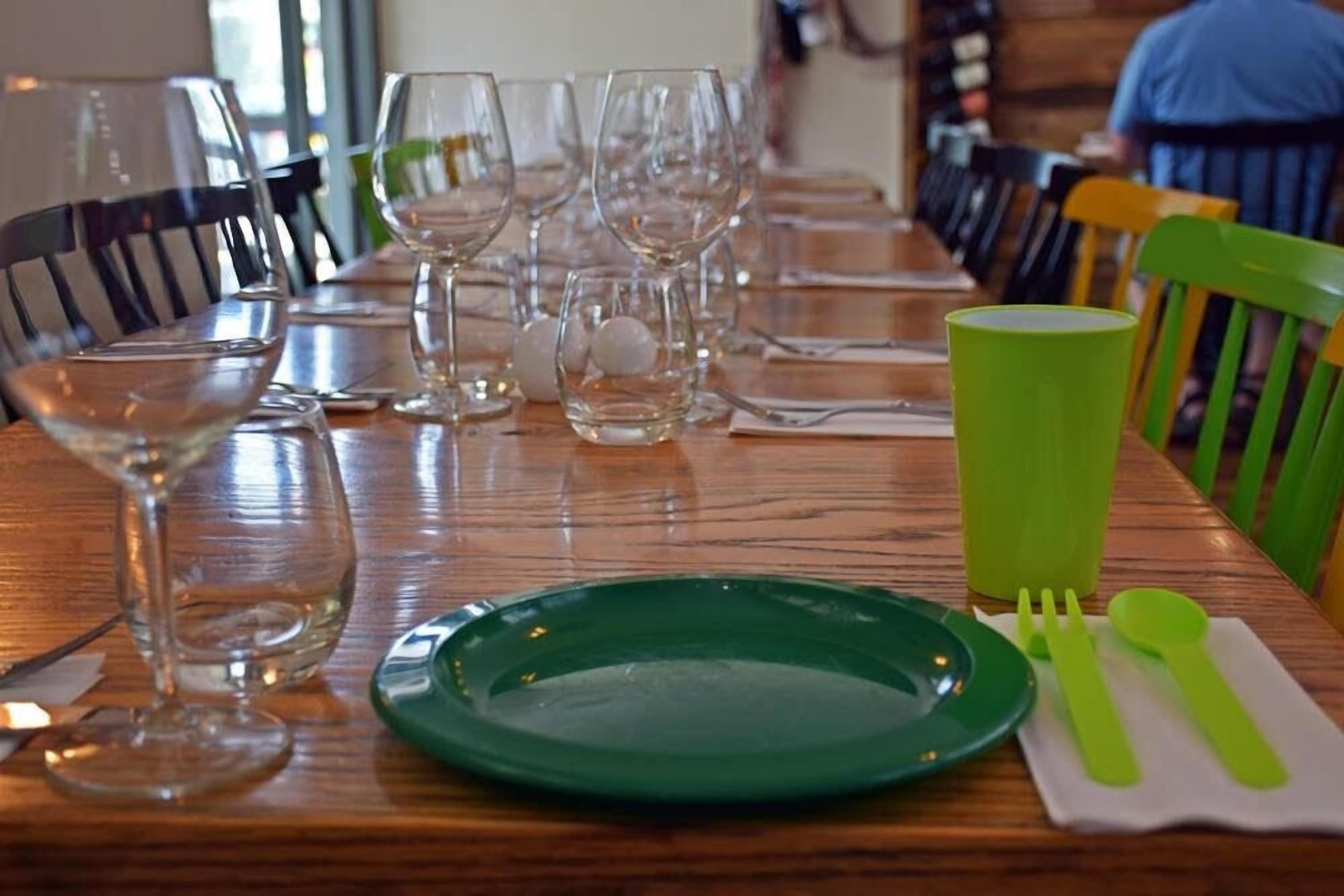 Una mesa de comedor dispuesta con vasos transparentes, un plato verde y cubiertos verdes.