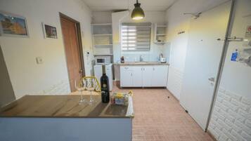 A compact kitchen with white cabinets, a wooden countertop, a hanging light fixture, and a microwave.