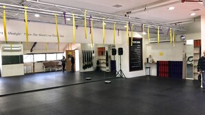 Un vaste espace d’entraînement intérieur doté de sangles suspendues de couleur jaune et violette, d’un sol recouvert de tapis noirs et d’un mur miroir.