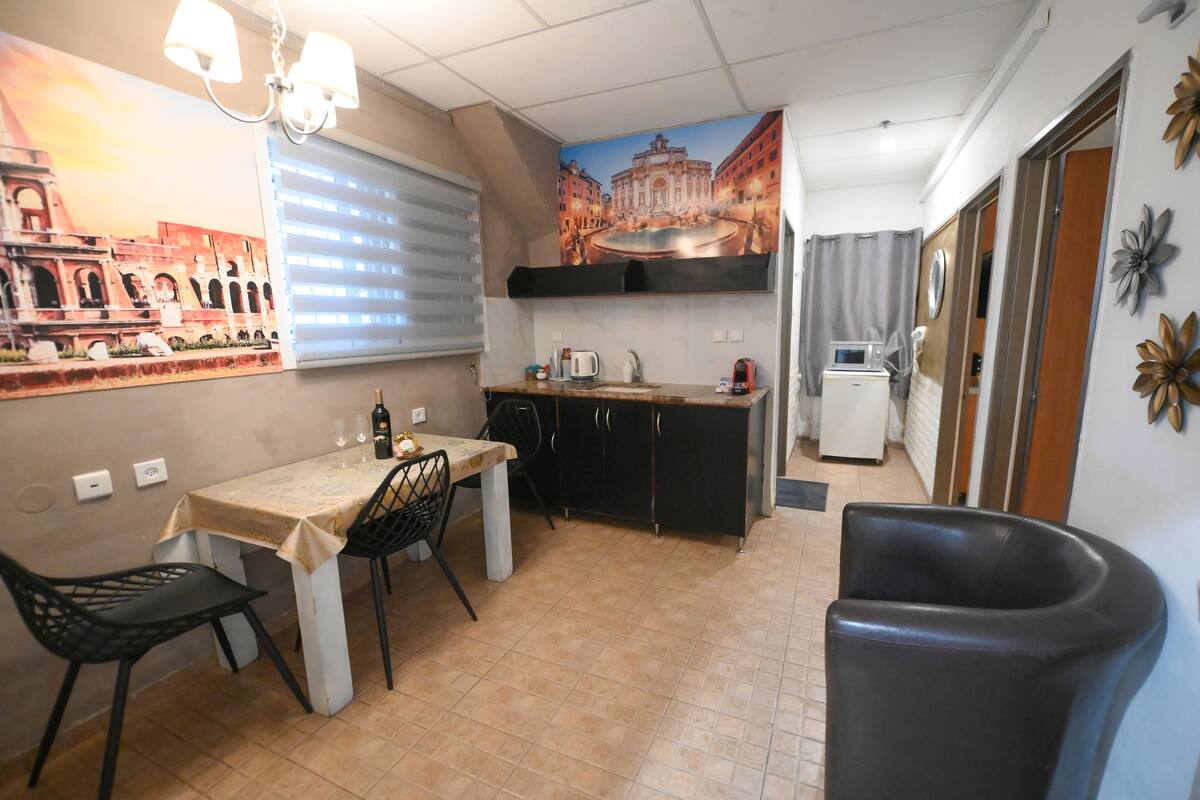 Uma cozinha compacta com mesa, cadeiras, geladeira e micro-ondas.
