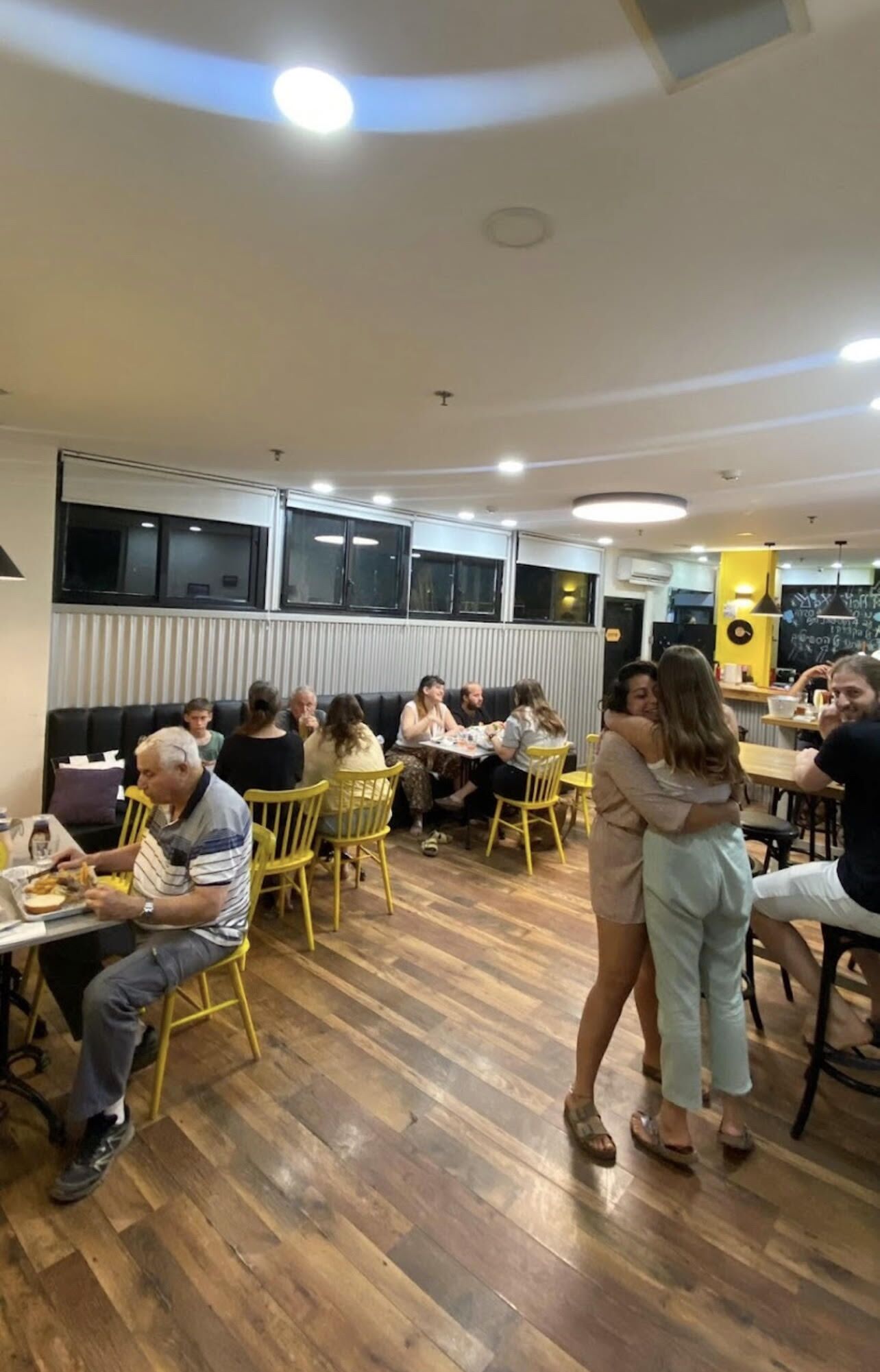 A restaurant with wooden flooring, yellow chairs, and a group of people dining.
