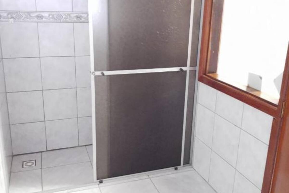 A small, enclosed shower area with tiled walls and floor, a window, and a wooden door.