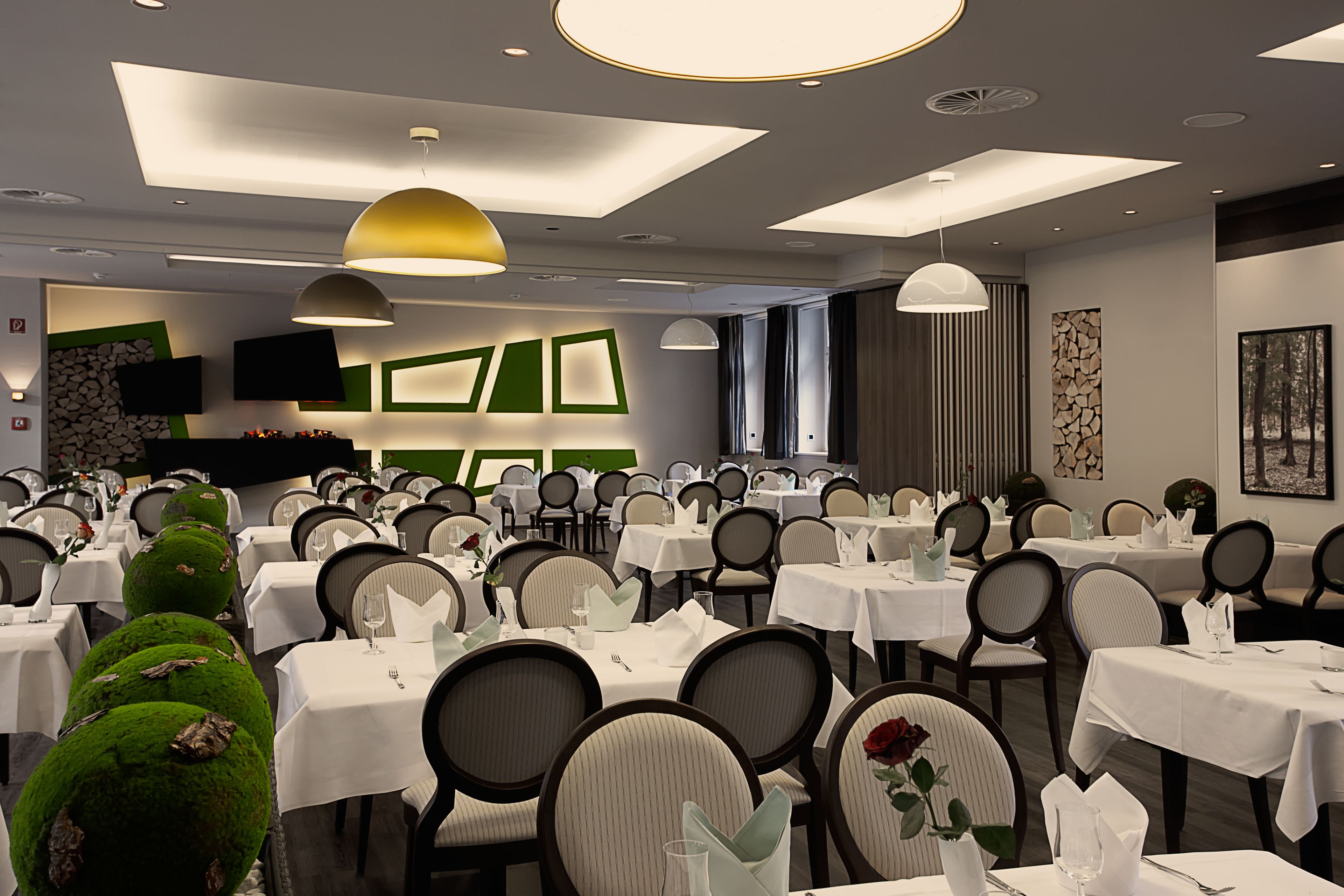 A dining area with multiple tables and chairs, a flat-screen TV mounted on the wall, and a modern ceiling design with recessed lighting.