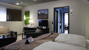 Una habitación de hotel moderna con una cama, un escritorio con una computadora, un televisor y una decoración de pared verde.