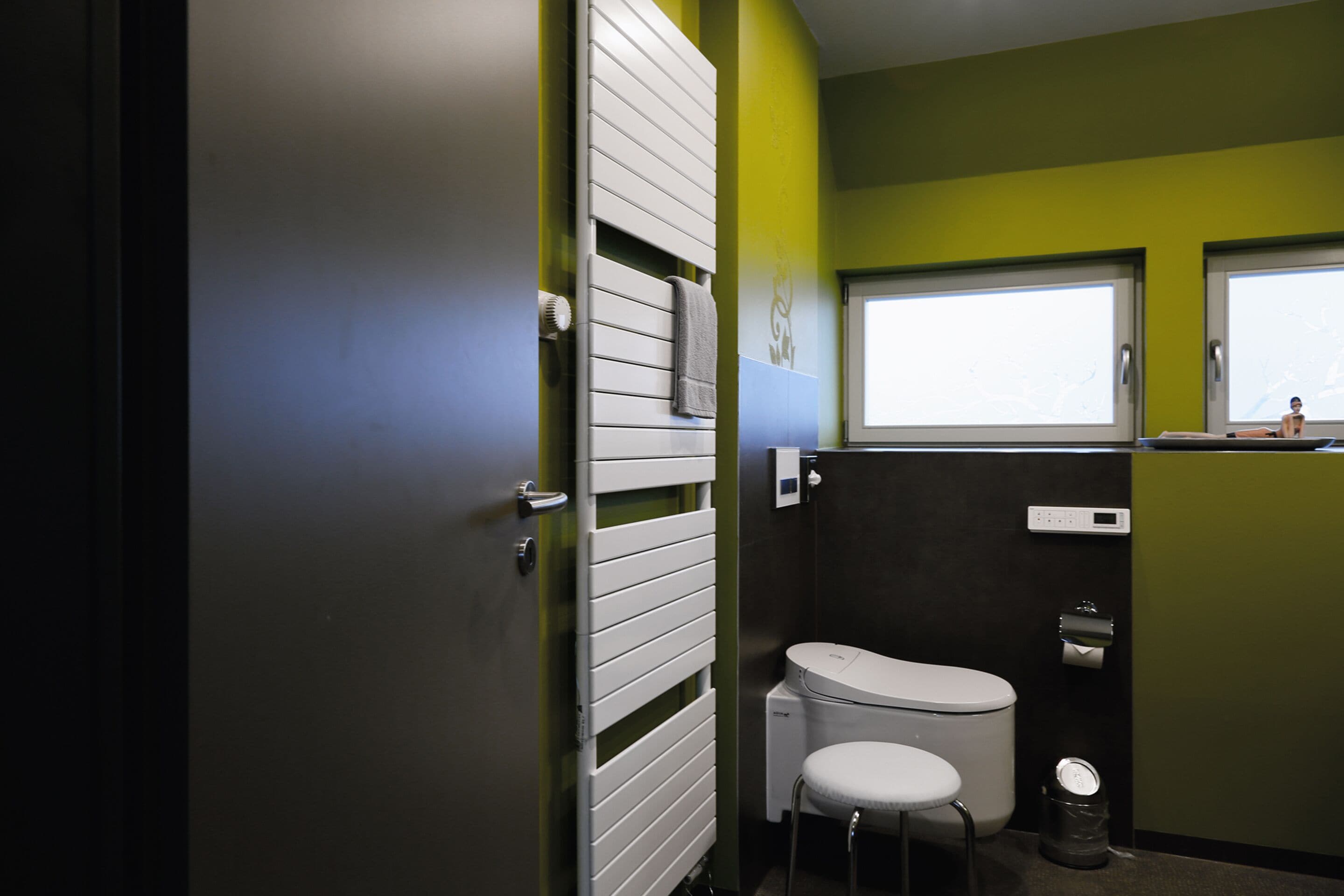 Une salle de bain avec des toilettes, un petit tabouret, une fenêtre et un radiateur.