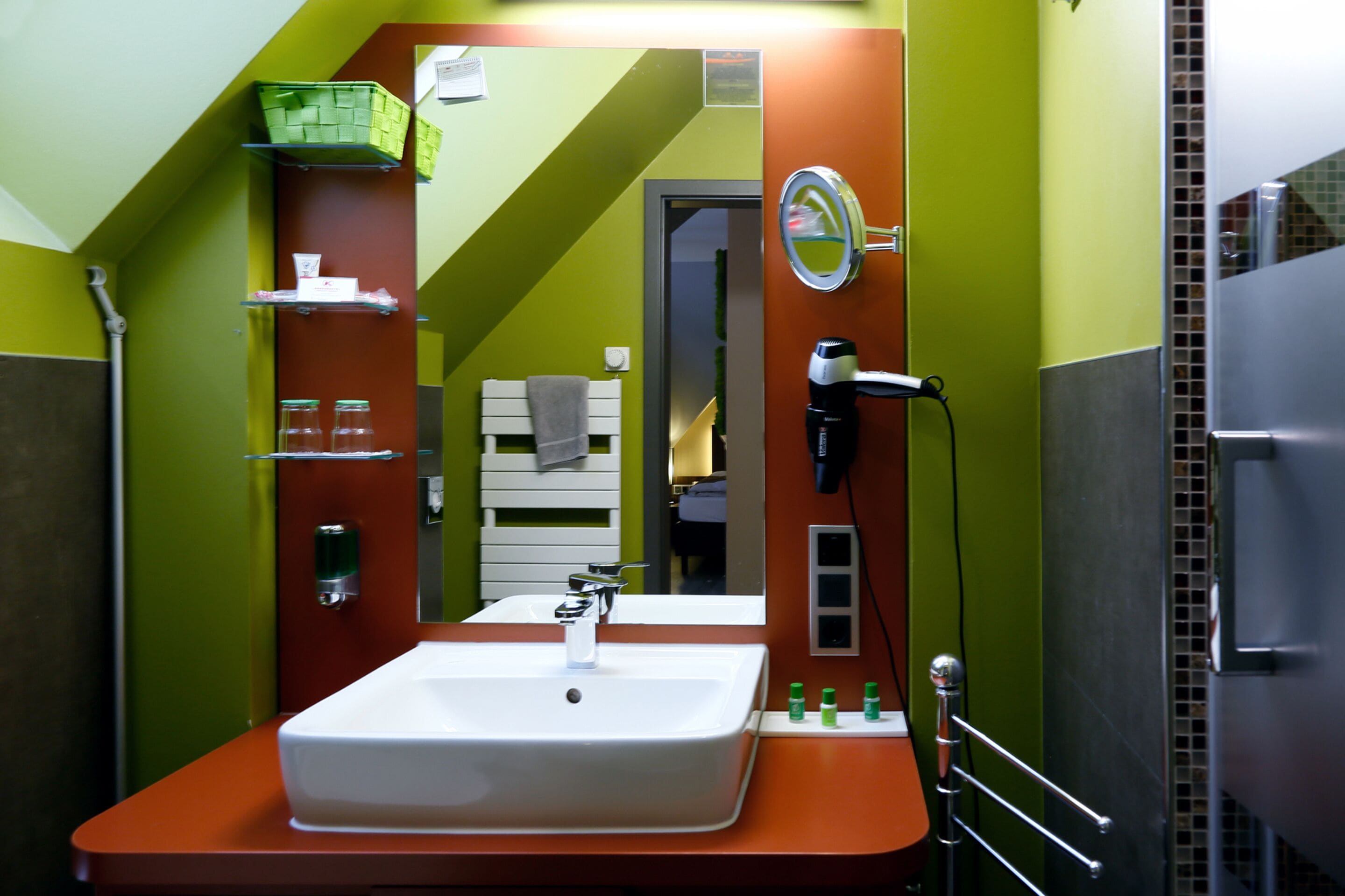 Een badkamer met een witte wastafel, groene wanden en een spiegel.
