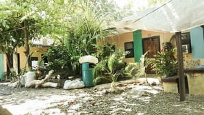 A courtyard with a building, potted plants, and a trash bin. - Hotel Economico (Roatan)