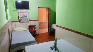 A small room with two beds, a chair, a table, a TV, and a door leading to another room. - Hotel Economico (Roatan)