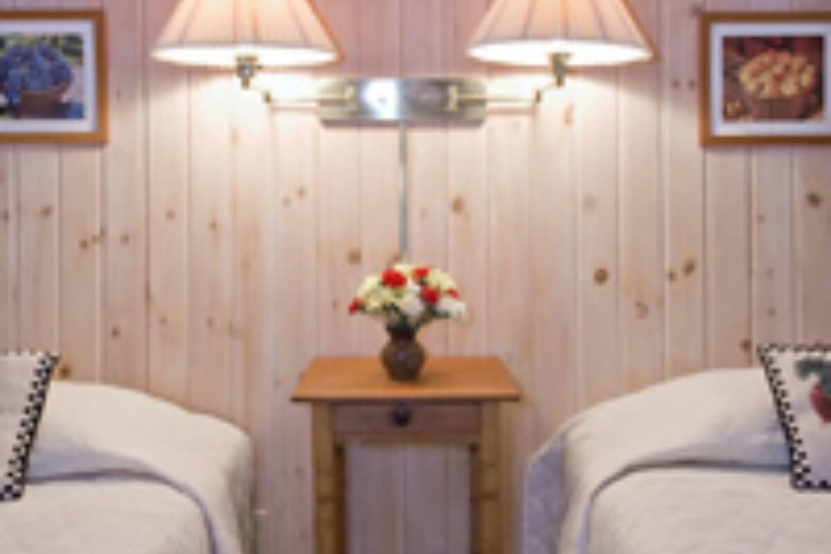 A room with two beds, a small table with a vase of flowers, and wall-mounted lamps.