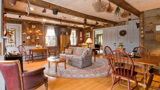 A cozy, rustic room with wooden floors, a round coffee table, a sofa, and a dining table with chairs. - The Waterford Inne (Waterford)