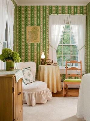 A cozy room with a green and white patterned wallpaper, a wooden chair, a small table with a lamp, and a window with curtains. - The Waterford Inne (Waterford)