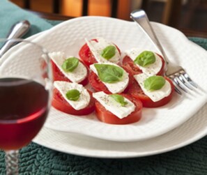 A plate of tomato slices topped with cheese and basil, accompanied by a glass of red wine and a fork. - The Waterford Inne (Waterford)