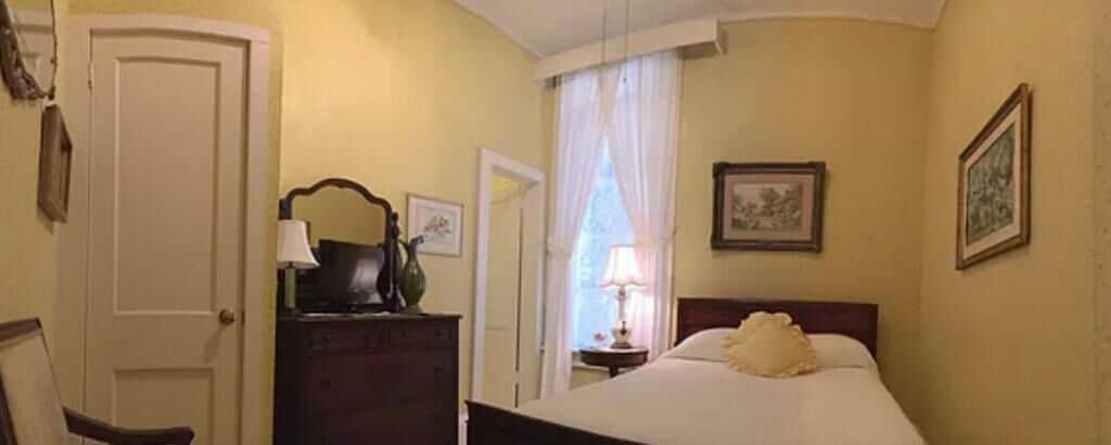 Una habitación de hotel con cama, cómoda, puerta y ventana con cortinas.
