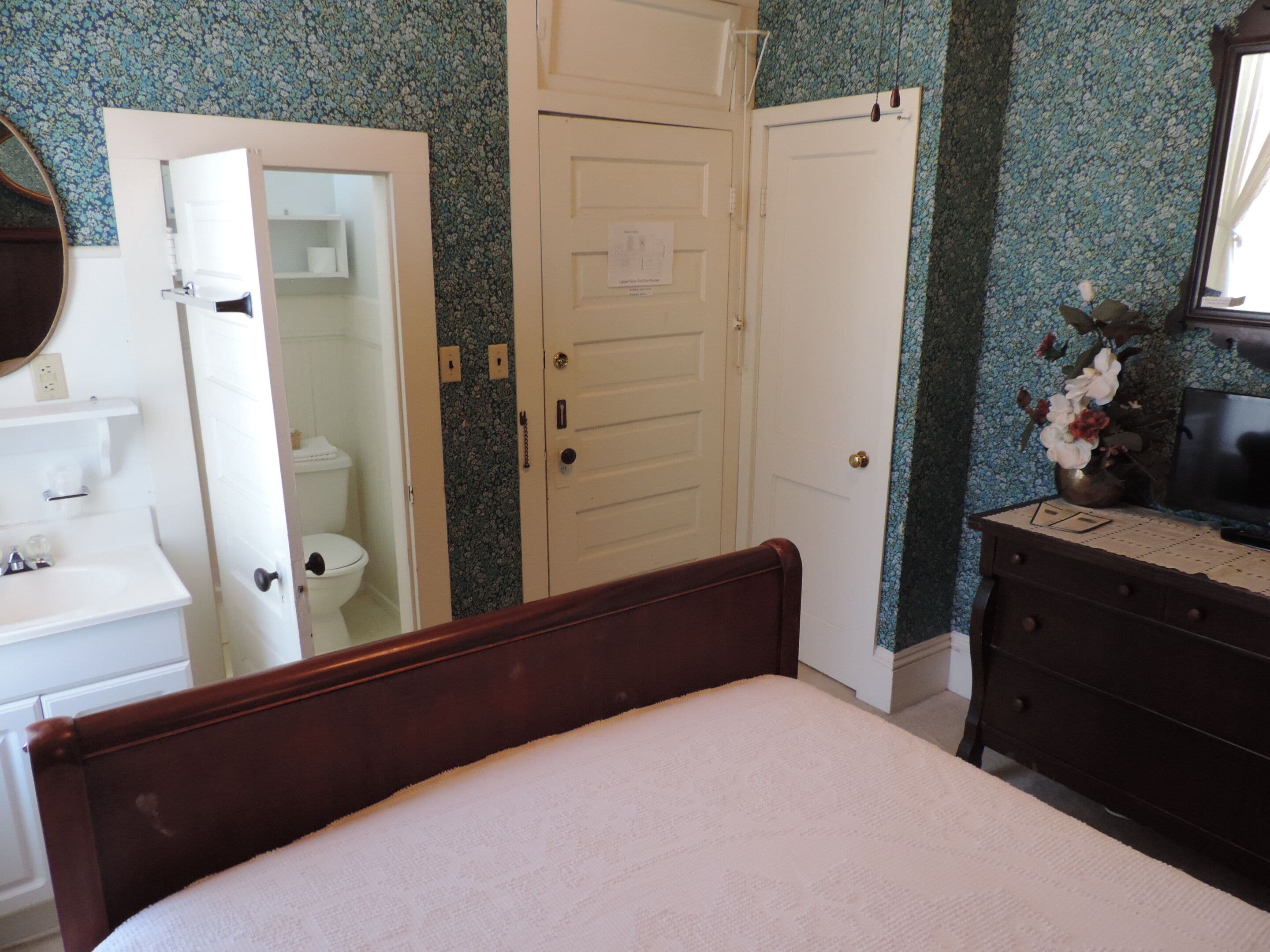A bedroom with a bed, a dresser, a mirror, and a door leading to a bathroom.