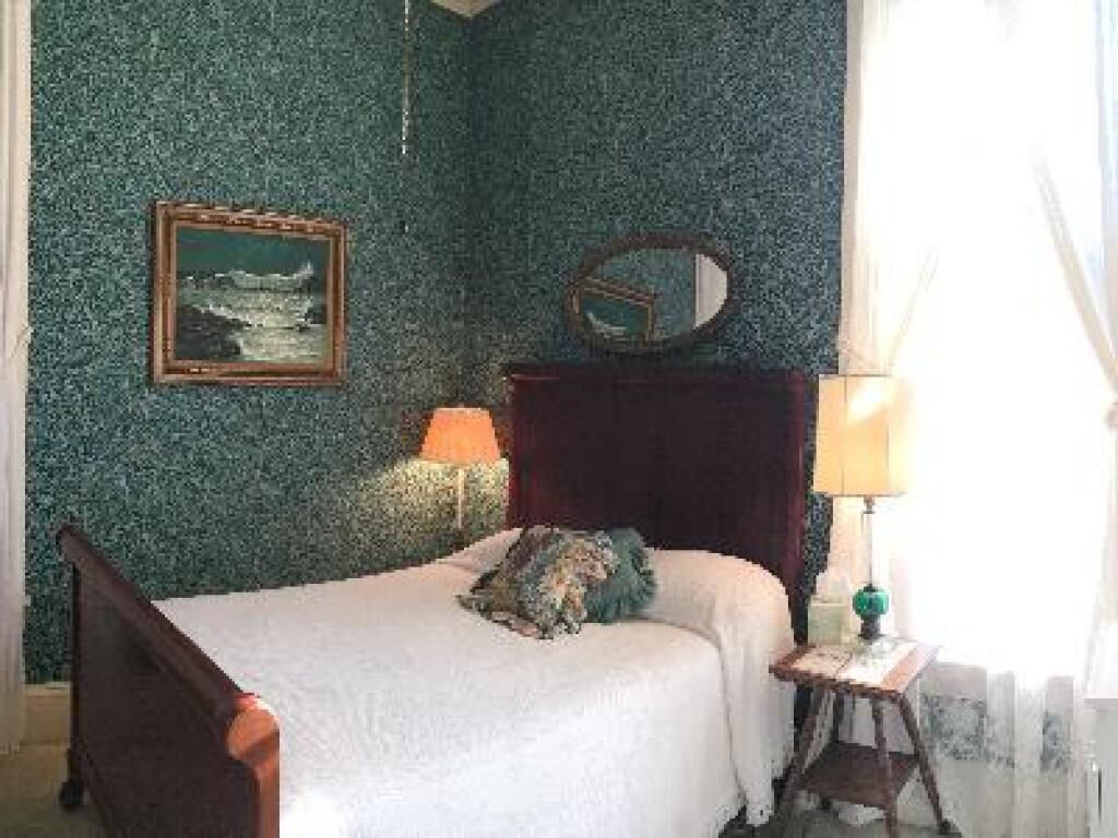 Un dormitorio con cama, mesita de noche, lámpara, espejo y un cuadro en la pared.