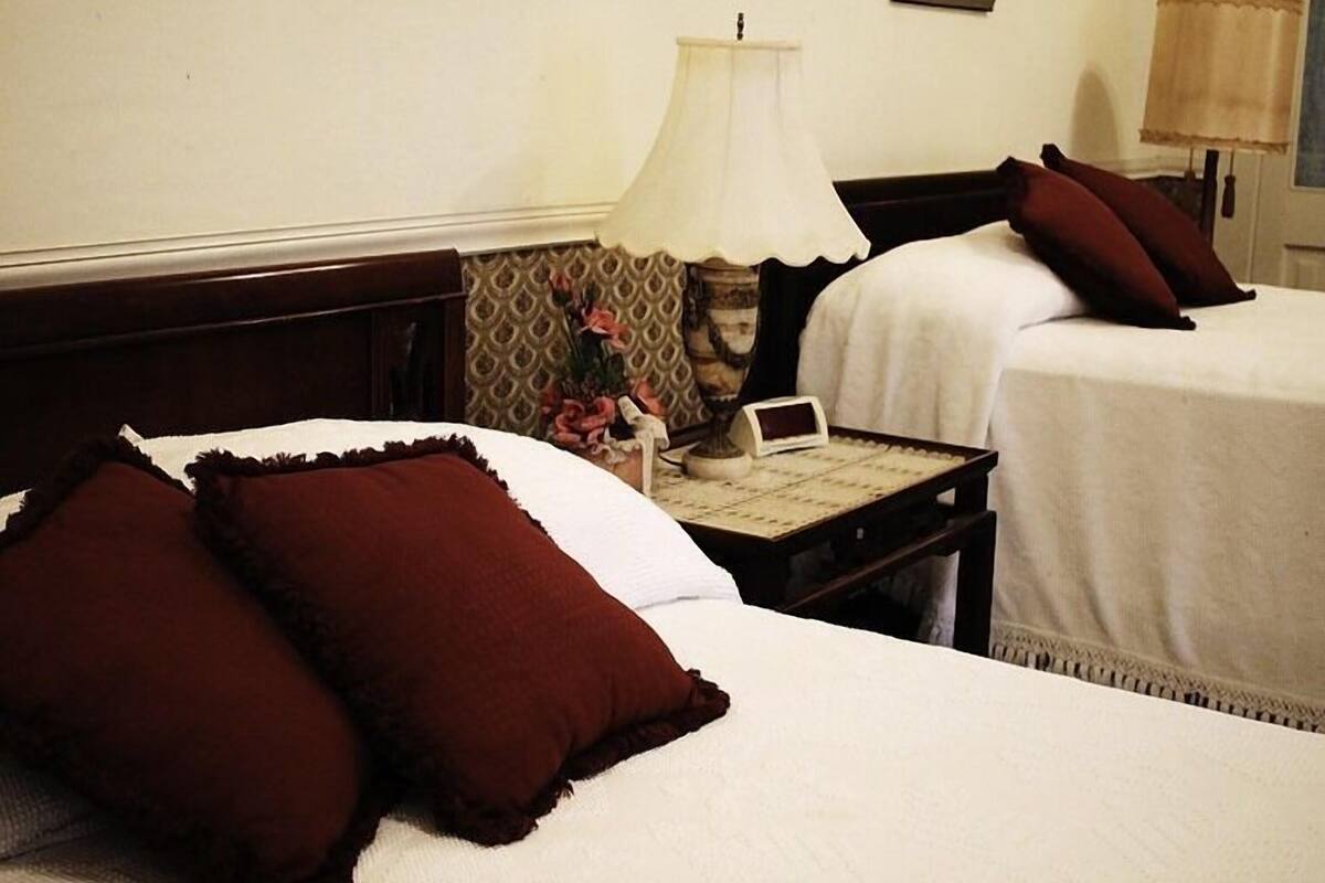 A hotel room with two beds, a nightstand with a lamp, a small table, and a framed picture on the wall.