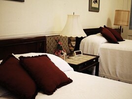 A hotel room with two beds, a nightstand with a lamp, a small table, and a framed picture on the wall.