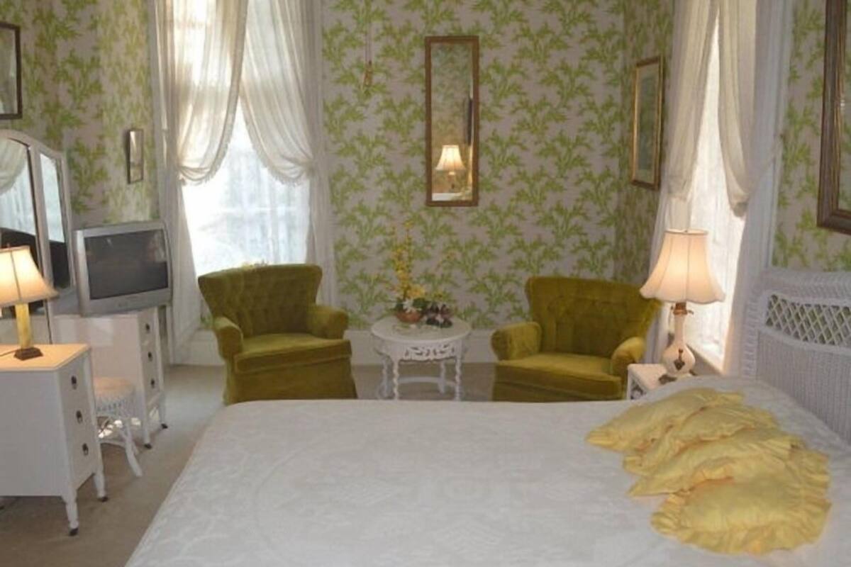 A hotel room with a bed, two armchairs, a small table, a television, and a lamp.