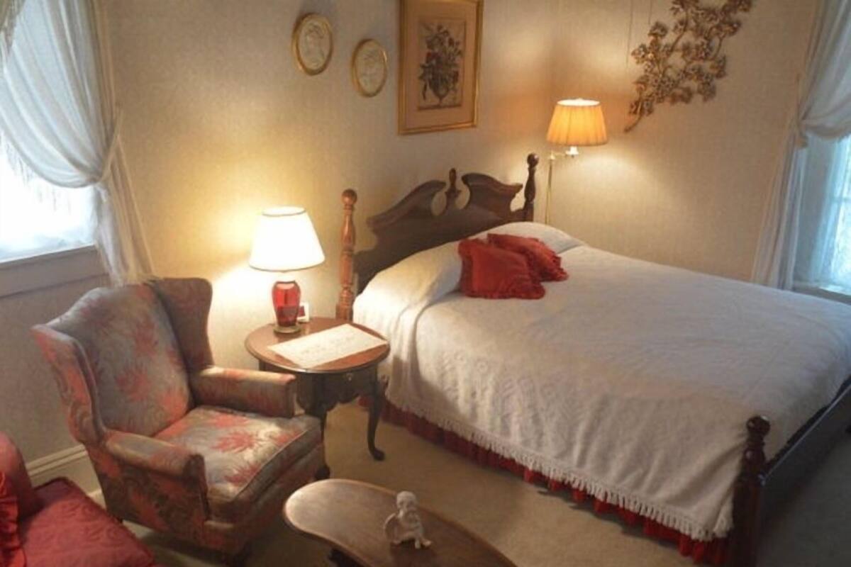 A bedroom with a bed, a chair, a small table, and a lamp.