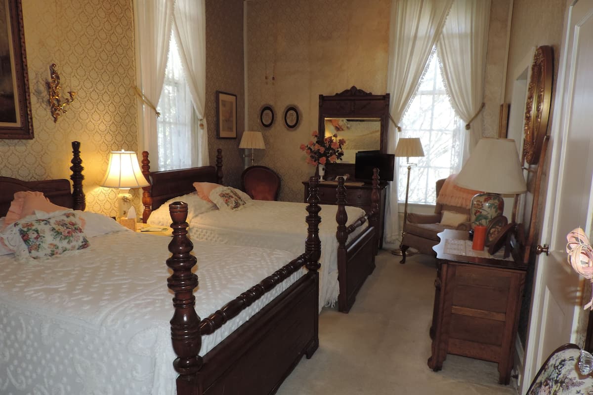 A traditional bedroom with a four-poster bed, a wooden dresser, and a chair.
