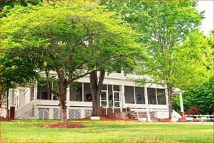 A white house with a porch, surrounded by trees.