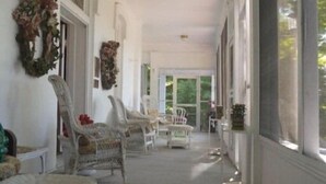 A covered porch with white wicker chairs, a dining table, and a large window providing a view of the outdoors. - Franklin Terrace Bed and Breakfast (Franklin)