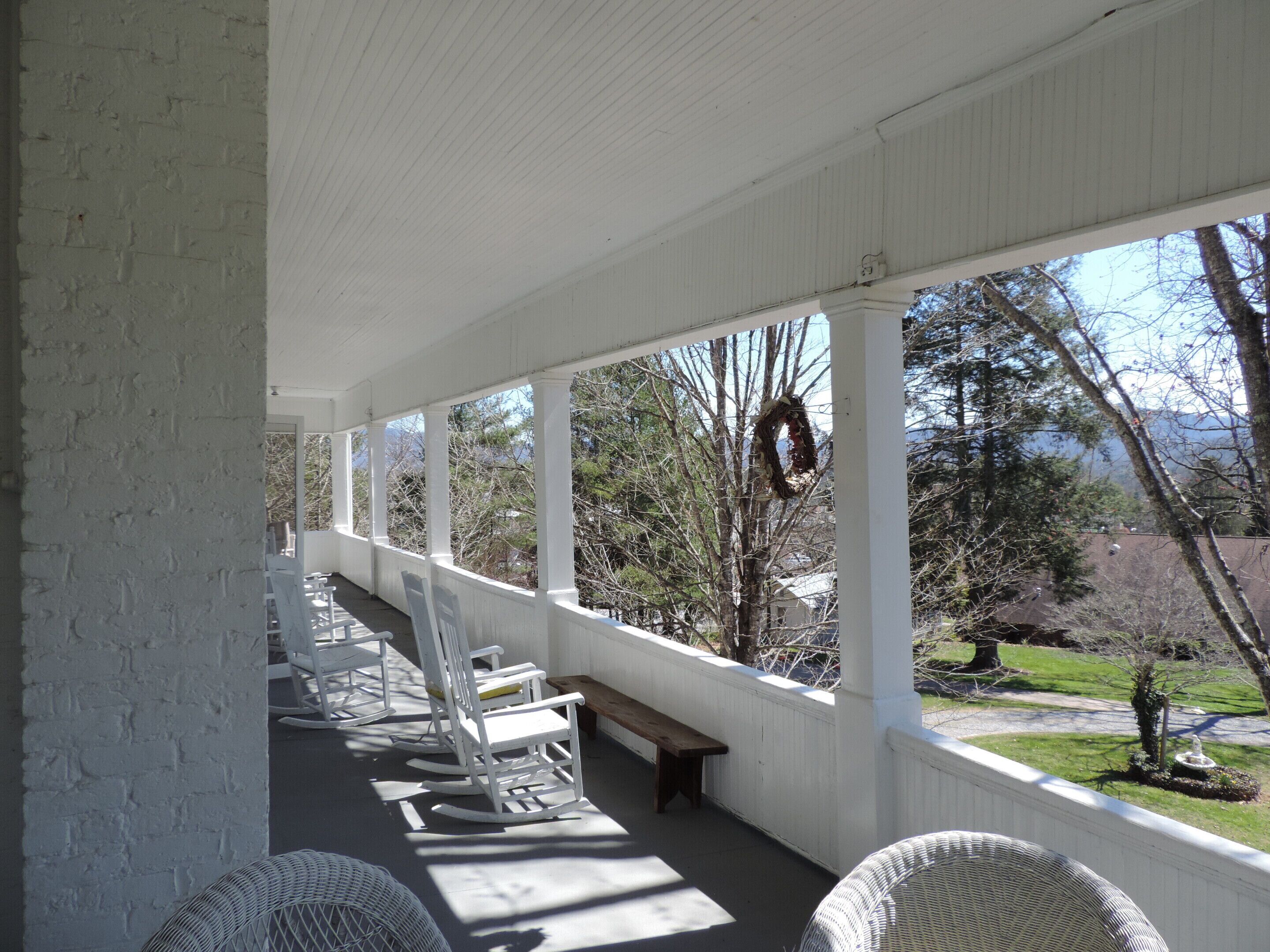 A covered porch with white columns, rocking chairs, and a bench.