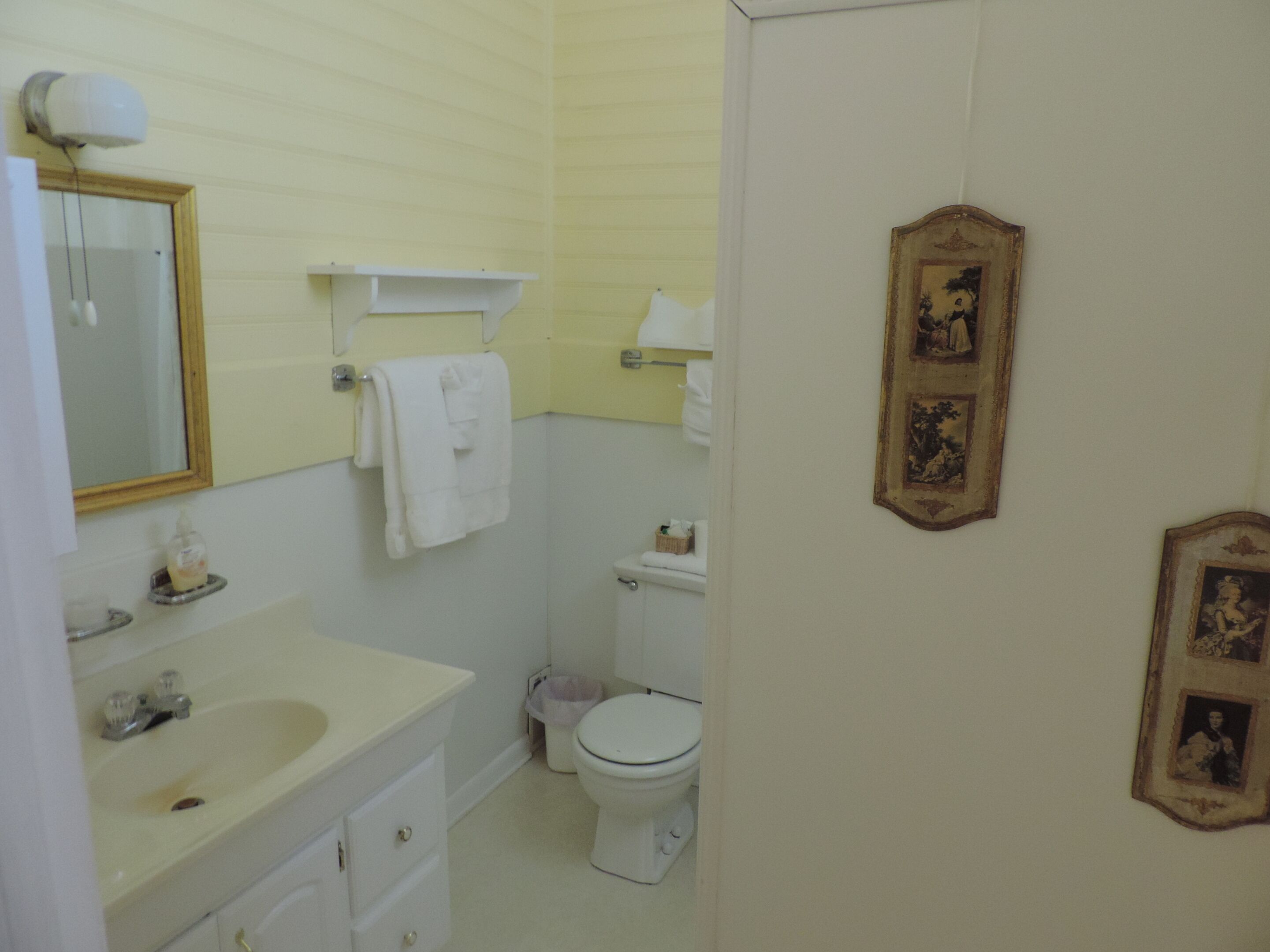 A small bathroom with a sink, mirror, towel rack, toilet, and framed pictures on the wall.