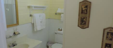 A small bathroom with a sink, mirror, towel rack, toilet, and framed pictures on the wall.