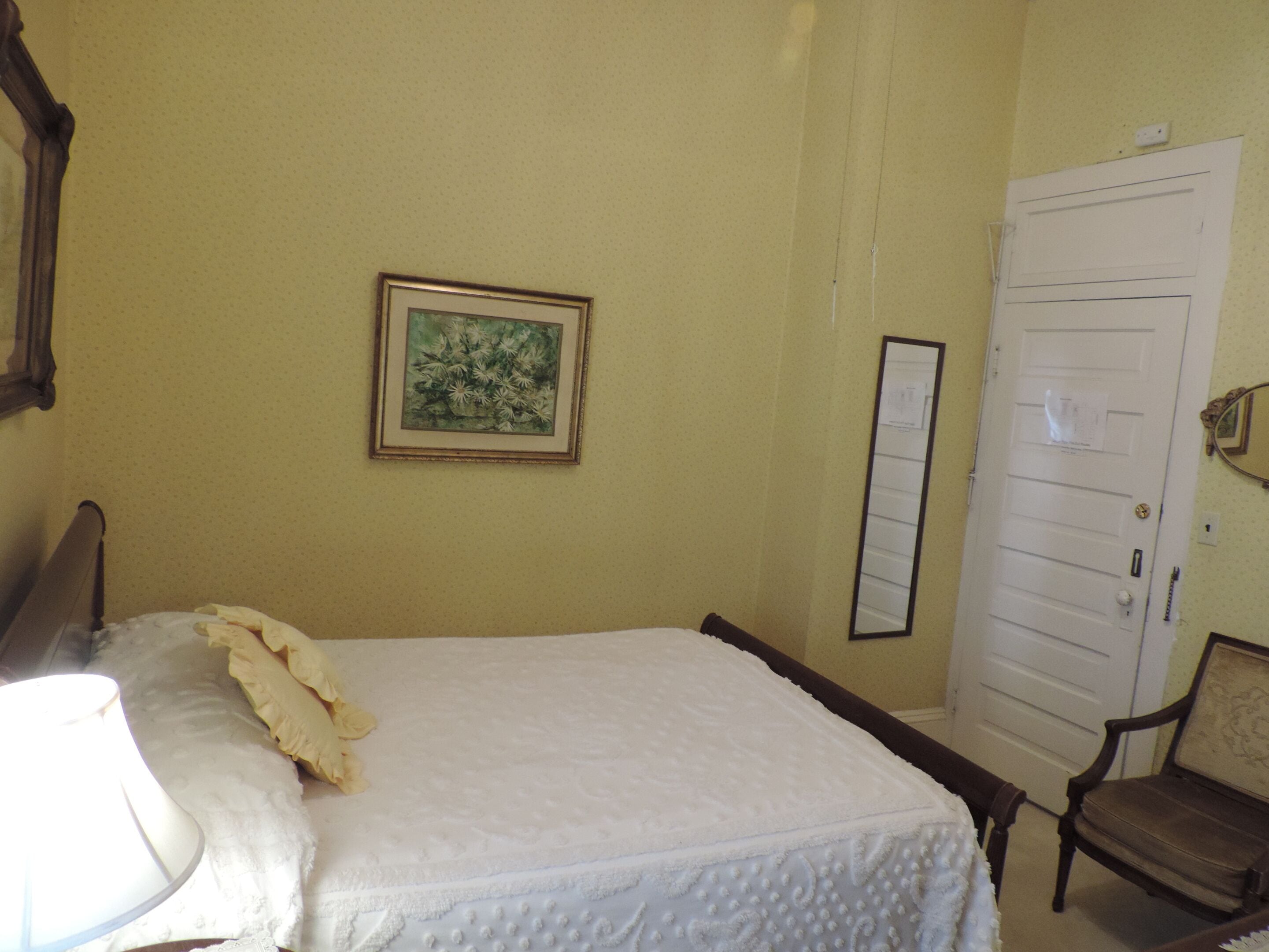 A bedroom with a bed, a chair, a door, and a framed picture on the wall.