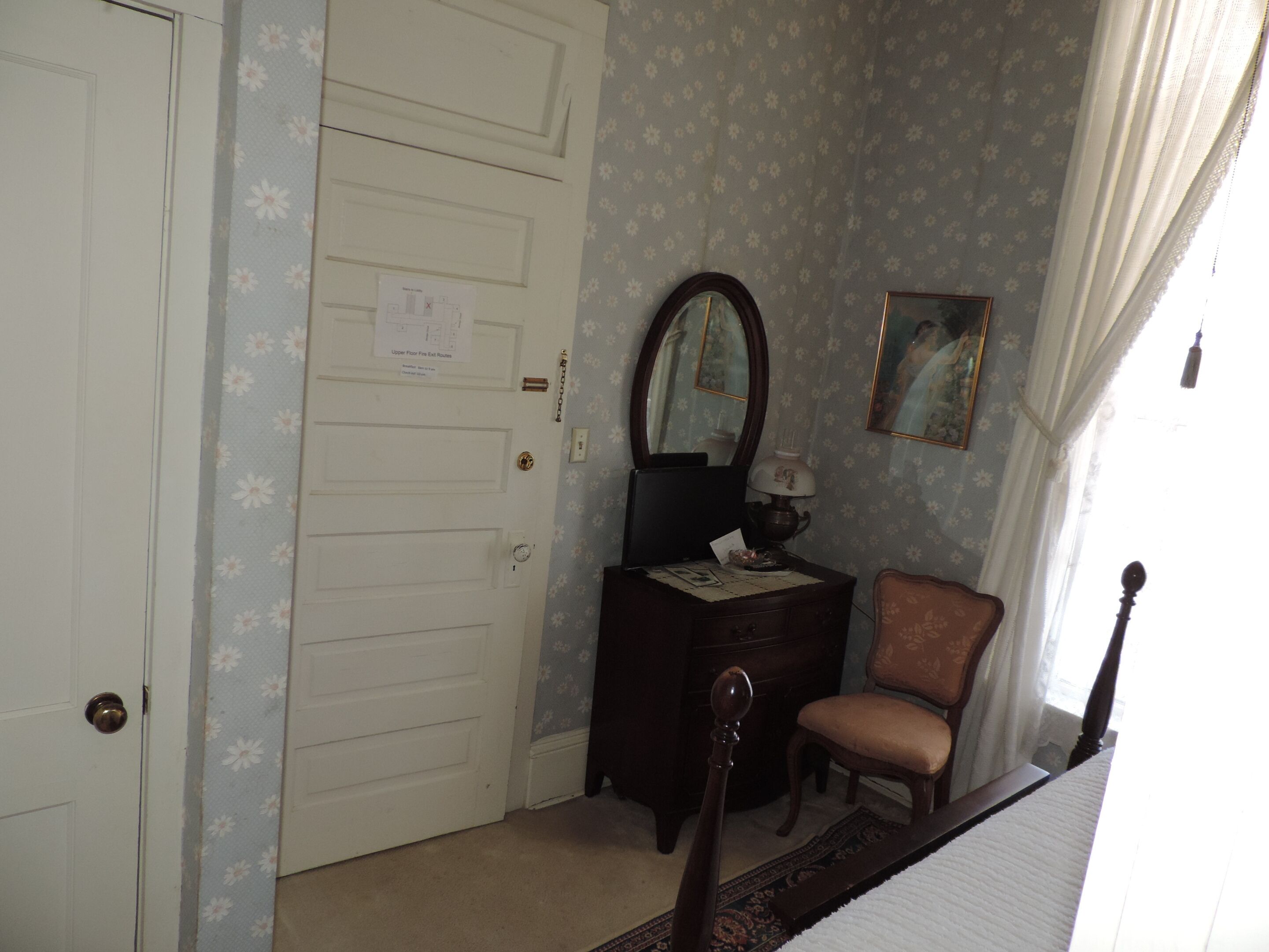 A bedroom with a closed door, a dresser with a mirror, a chair, and a bed.